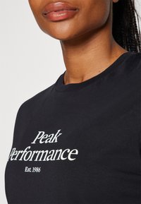 Czarna bawełniana koszulka z nadrukiem "Peak Performance" w białym kolorze, z okrągłym dekoltem i krótkimi rękawami.