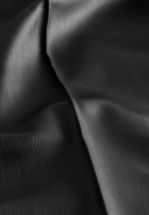Schwarzer, texturierter Kunstlederstoff, der eine glatte Oberfläche mit feiner Körnung zeigt, gefaltet, um Tiefe und sanfte Kurven zu offenbaren.