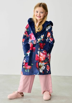 Navy kimono s cvjetnim uzorkom s mekanom kapuljačom, dubokim rukavima i pojasom, u kombinaciji s širokim svijetlopinkastim hlačama i ružičastim natikačama.