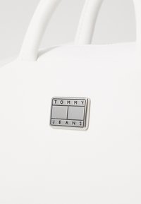 Borsa bianca in pelle liscia. Presenta due manici e una placca loghi rettangolare argento con la scritta "TOMMY JEANS" incisa.