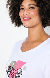 T-shirt blanc avec un graphique de tigre coloré, des formes abstraites en rose et gris, et un design de projection subtile. Texture en coton lisse.