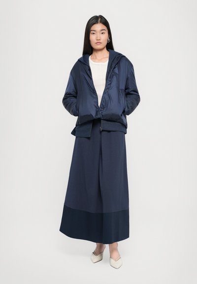 Morska zimska jakna s kapuco, skrajšana, v kombinaciji z dolgo morsko krilo z kontrastnim robom. Gladka tekstura, brez vidnih vzorcev ali podrobnosti.