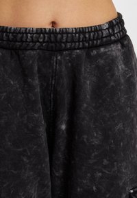 Svarte joggebukser med en teksturert, marmorert mønster. Har en tettsittende midje med en rynket elastisk design for komfort.