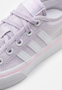 Lila canvas sneaker med vita tre ränder, gummisula och ljusrosa detaljer på sulan. Platta snören och runda hål kompletterar designen.