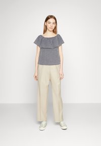 Haut décontracté à rayures bleu et blanc, avec un design volanté, associé à un pantalon large beige et des baskets claires.