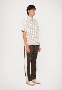 Kortermet kremfarget skjorte med brun "ISKREM"-mønster, kombinert med brune sateng joggebukser med hvite sidestriper og hvite sneakers.