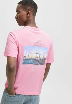 Lyserød bomulds T-shirt med et grafisk print på ryggen, der viser en solnedgang over en basketballbane og tekstinformationer under billedet.