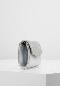 Stříbrná metalická kabelka typu clutch s třpytivým klopem, vyznačující se hladkým povrchem a zaobleným tvarem, vhodná pro formální příležitosti.