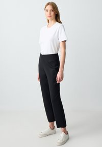 T-shirt blanc à manches courtes associé à un pantalon noir ajusté et des baskets blanches. Design à jambe droite avec une texture de tissu lisse.