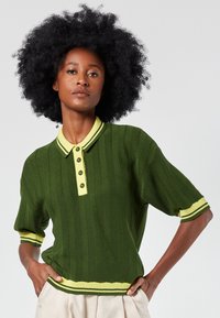 Green knitted polo shirt with a yellow collar, four-button placket, and striped cuffs. Features a textured, ribbed pattern throughout.