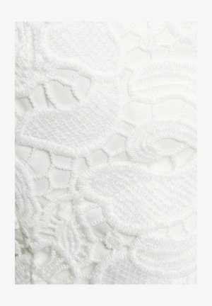 White fabric with intricate embroidered lace design featuring floral patterns and smooth, textured accents. Detailed stitching on a sheer background.
