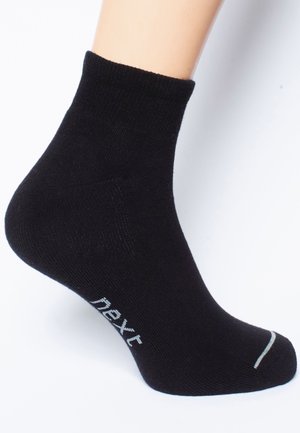 Schwarze Knöchelsocke aus weichem, elastischem Material mit geripptem Bündchen. Verfügt über hellgrauen Logo-Text und Akzentstreifen an der Zehenspitze.