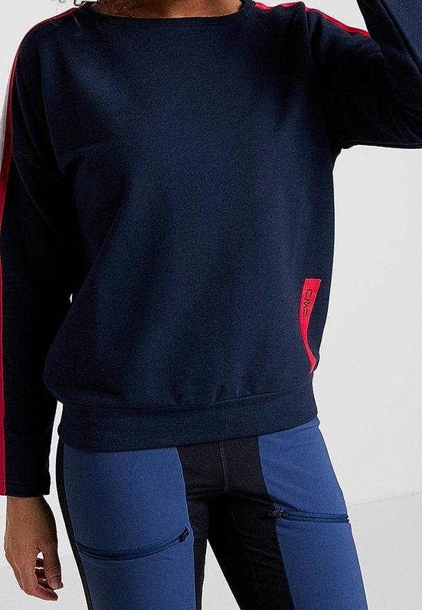 Personne portant un sweat-shirt bleu marine avec une bande rouge sur les manches et un pantalon assorti bleu avec des poches zippées noires.