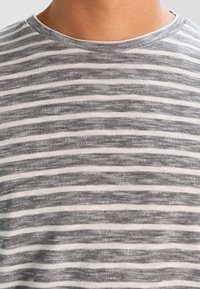T-shirt a righe grigie e bianche con scollatura rotonda, realizzata in tessuto morbido. Le righe sono distanziate uniformemente, con un aspetto leggermente strutturato.