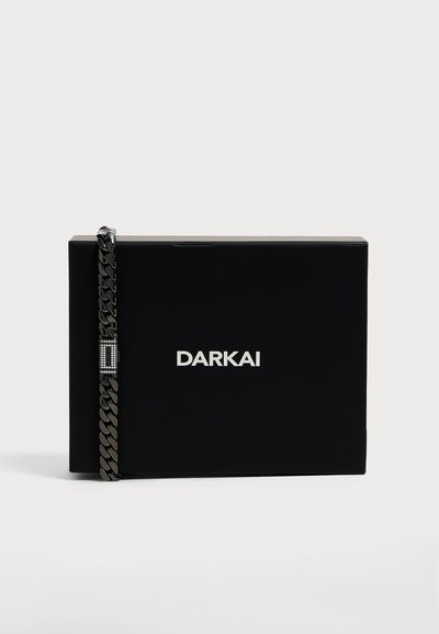 Μαύρο ορθογώνιο κουτί με λευκό λογότυπο DARKAI, συνοδευόμενο από μαύρο βραχιόλι αλυσίδα με ορθογώνια πόρπη διακοσμημένη με στρας.