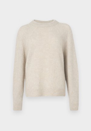 Beige kudumiigiga särk, millel on ümar kaelus, raglanvarrukad ja soonik. Pehme tekstuur, veidi avar istuvus ja minimaalne muster.