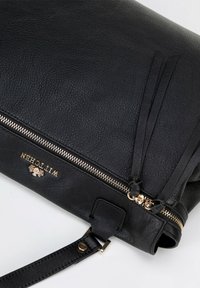 Borsa a tracolla in pelle nera con una superficie texturizzata, hardware dorato, chiusura con zip e nappine decorative in pelle. Presenta una tracolla removibile.