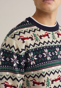 Suéter de punto con base color crema y acentos en azul marino. Los patrones incluyen zorros rojos, árboles verdes y copos de nieve blancos, junto con diseños de zigzag.