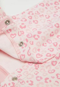 Różowa tkanina z wzorem w serca i zwierzęta. Zapinana na napy, z miękką podszewką i ściągaczami.