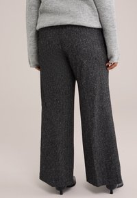 Weite Hosen aus strukturiertem schwarzem Stoff mit subtilen silbernen Sprenkeln. Mit hoher Taille und glattem Rücken, kombiniert mit schwarzen Schuhen.