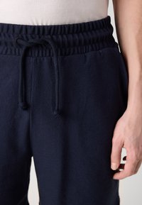 Pantalones jogger de algodón azul marino con una cintura de canalé, cordón ajustable y textura suave. Mano parcialmente visible en el lateral.