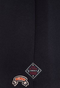 Tissu de sweat-shirt bleu marine foncé avec une texture lisse. Présente un logo en diamant brodé et un patch en ruban avec le mot "BLAUW."