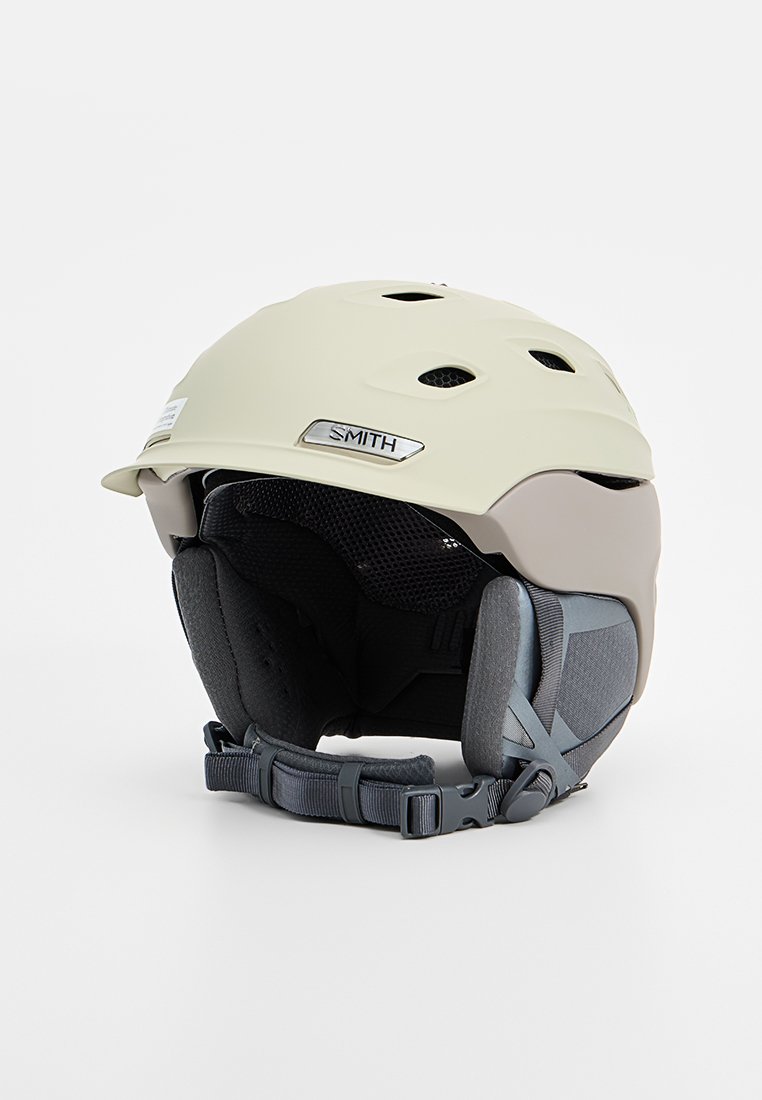 Kask narciarski Smith w jasnym beżu i szarości, z otworami wentylacyjnymi, wyściółką oraz regulowanymi paskami dla pewnego dopasowania.