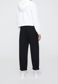 Bílá zkrácená bunda s kapucí, v kombinaci s černými volnými kalhotami. Celý outfit doplňují bílé tenisky a ohrnuté manžety.