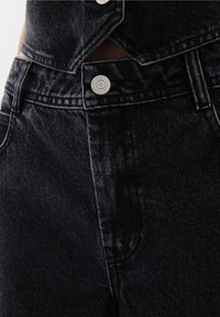 Zwarte spijkerbroek van denim met een hoge tailleband, zilveren knoopsluiting en een gestructureerde stof met een lichte glans. Close-up van de voorkant.
