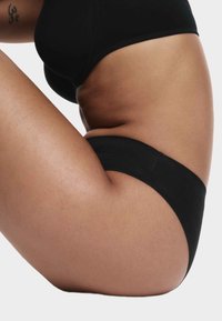 Tanga nero con una superficie liscia, caratterizzato da un taglio a vita bassa. L'elastico è semplice, senza marchi o decorazioni visibili.