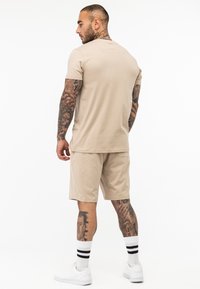Set dintr-un tricou și șort din bumbac bej, cu mâneci scurte și o croială lejeră. Accesorizat cu șosete albe cu dungi negre și adidași albi.