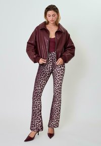 Giacca in ecopelle bordeaux con un grande colletto, abbinata a pantaloni a palazzo a vita alta con stampa leopardata e décolleté bordeaux a punta.