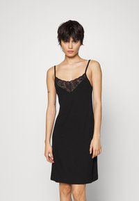 Abito nero aderente realizzato in tessuto morbido con dettagli in pizzo sullo scollo. Presenta spalline sottili e una vestibilità rilassata.