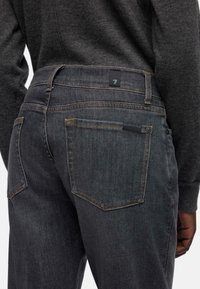 Ciemnoszare dżinsy o teksturowanym wykończeniu, z pomarańczowym przeszyciem, dwoma tylnymi kieszeniami oraz czarną metką na pasku talii.