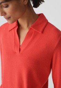 Koraalrode pullover met een zachte textuur, voorzien van een V-hals en een gestructureerde kraag. Eenvoudig, gestroomlijnd ontwerp met lange mouwen.