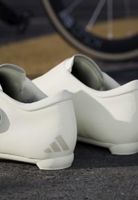 Weiße Fahrradeschuhe mit einer glatten synthetischen Außenseite, strukturierten Akzenten und einem grauen Drei-Streifen-Logo an der Ferse. Abgerundete Zehenform.