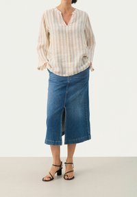 Blusa di lino a righe beige e bianche con scollatura a V e maniche lunghe, abbinata a una gonna di jeans blu con spacco frontale. Sandali neri con tacco.