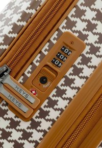 Valigia rigida con un motivo a scacchiera marrone e bianco, zip marrone e una serratura a combinazione con tre dischi e logo TSA.