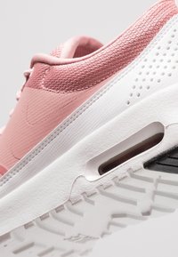 Zapatillas de aire en color rosa claro y blanco, con tela texturada, diseño elegante, unidad de aire visible y una suela de goma resistente con patrones de tracción.