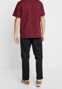 Camiseta de algodón burdeos, corte holgado, combinada con pantalones negros y zapatillas marrones y blancas. Diseño sencillo, sin logotipos ni patrones visibles.