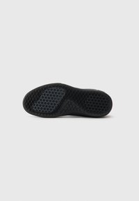 Black rubber shoe sole with a patterned grip, featuring geometric textures and a rounded shape, designed for enhanced traction.