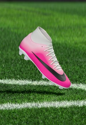 Pantof de fotbal roz și alb cu swoosh Nike negru plutind deasupra ierbii verzi cu linii albe de teren.