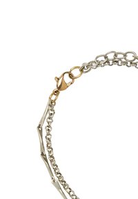 Bransoletka z mieszanych metali srebrnego i złotego z ogniwami połączonymi ze sobą, z zapięciem typu pazur oraz kanciastymi akcentami na niektórych ogniwach.