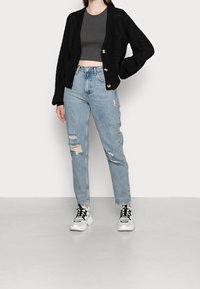 Svart stickad cardigan med ett strukturerat mönster, bärs över en grå crop top. Distressade ljusblå jeans med hål. Vita sneakers med svarta snörningar.