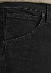 Czarne dżinsy o gładkiej fakturze, z przednią kieszenią i małą metalową metką z logo. Dyskretne szwy i klasyczny krój.