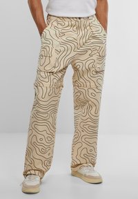 Beige cargo pants with black wavy line patterns, featuring multiple pockets and a relaxed fit, made of a smooth fabric.