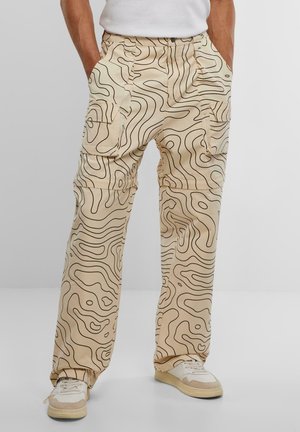 Beige cargo pants with black wavy line patterns, featuring multiple pockets and a relaxed fit, made of a smooth fabric.