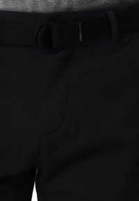 Pantalons noirs en tissu texturé, dotés d'une poche latérale et d'une ceinture noire avec une boucle circulaire. Design simple et fonctionnel.