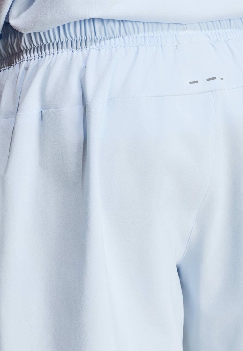 Primer plano de pantalones azul celeste con cintura elástica, detalles cosidos y un pequeño logo reflectante en el lado derecho.