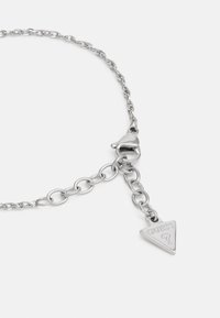 Pulseira de prata com um encantador triangular gravado com "GUESS" e uma chave, apresentando um acabamento liso e polido.